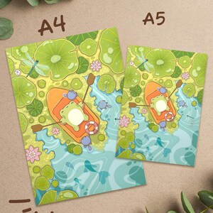 May include: Two art prints, A4 and A5 sizes, featuring a whimsical illustration of a frog in an orange boat on a pond. The scene includes lily pads, dragonflies, and fish, with the text "A4" and "A5" on the prints.