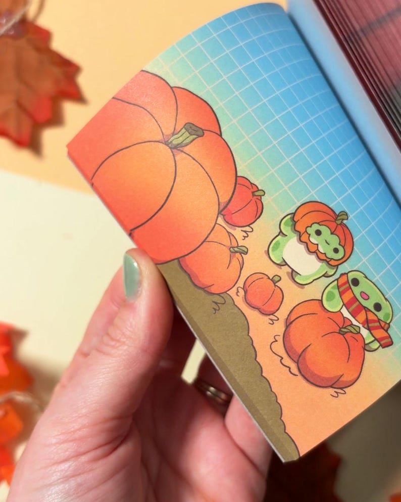 May include: A notepad page featuring a grid background with a gradient from blue to orange. The illustration shows several orange pumpkins and two small green creatures, one wearing a pumpkin hat and the other wearing a striped scarf.