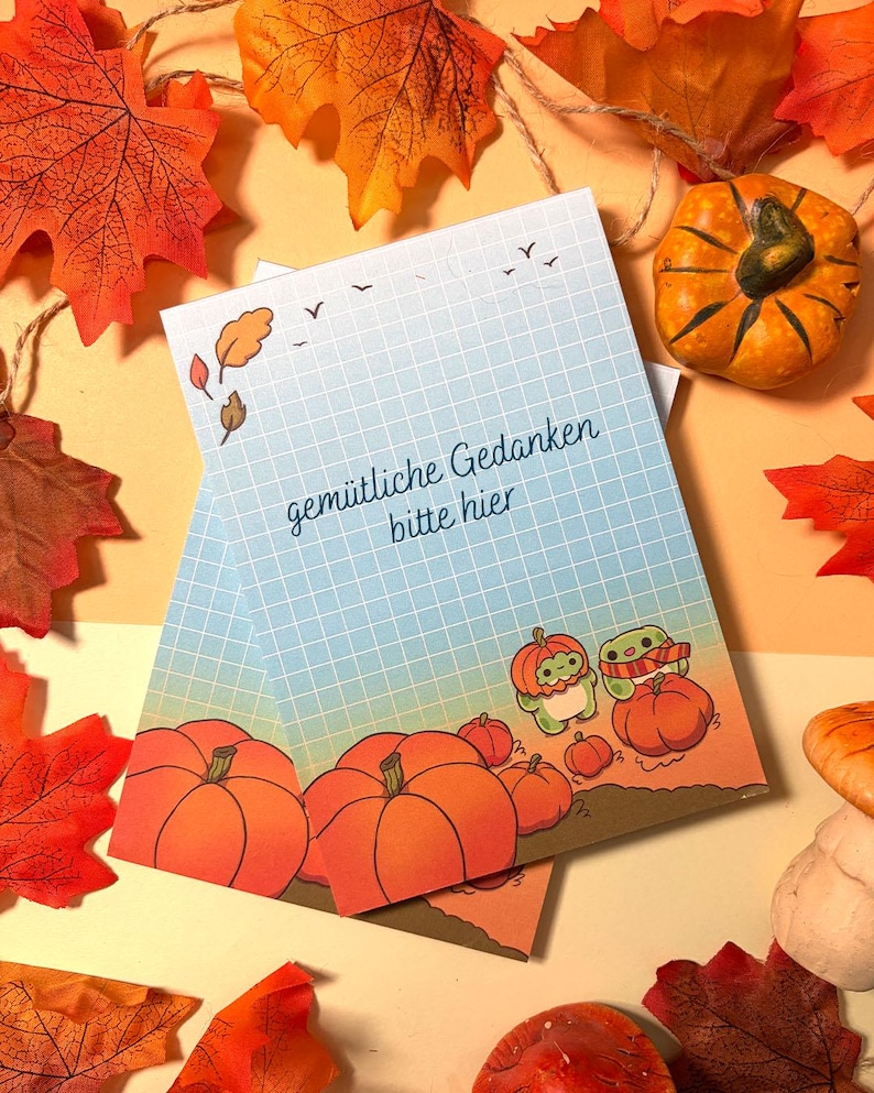 May include: A rectangular notepad featuring a light blue grid pattern, autumn leaves, and pumpkins. The text "gem&uuml;tliche Gedanken bitte hier" is printed in the center. Two small green creatures are illustrated wearing pumpkin hats.