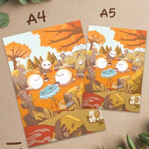 May include: Two art prints, labeled A4 and A5, feature a whimsical graveyard scene. The illustration showcases cartoon ghosts enjoying tea, surrounded by orange trees and tombstones. The color palette includes orange, brown, and light blue.