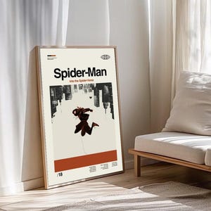 Puede incluir: Un p&oacute;ster enmarcado con el t&iacute;tulo "Spider-Man" y el subt&iacute;tulo "Into the Spider-Verse". El p&oacute;ster muestra un paisaje urbano y una figura de Spider-Man sobre un fondo beige. El marco es de madera clara. El p&oacute;ster est&aacute; apoyado contra una pared.