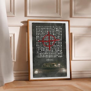 Puede incluir: Póster enmarcado con un código críptico y un símbolo de mira roja. La palabra "ZODIAC" está en la parte inferior, con una imagen de un coche antiguo. El póster está en un marco de madera, apoyado contra una pared.