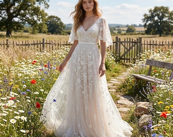May include: A floor-length white dress featuring a V-neckline, flutter sleeves, and a fitted waist. The dress is adorned with intricate white floral embroidery over a light beige base, with a flowing skirt that reaches the ground.