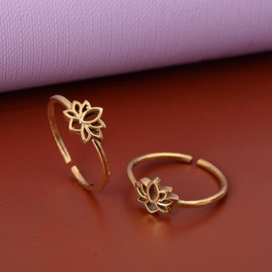 May include: Two gold-toned toe rings featuring a lotus flower design. The rings are open and adjustable.