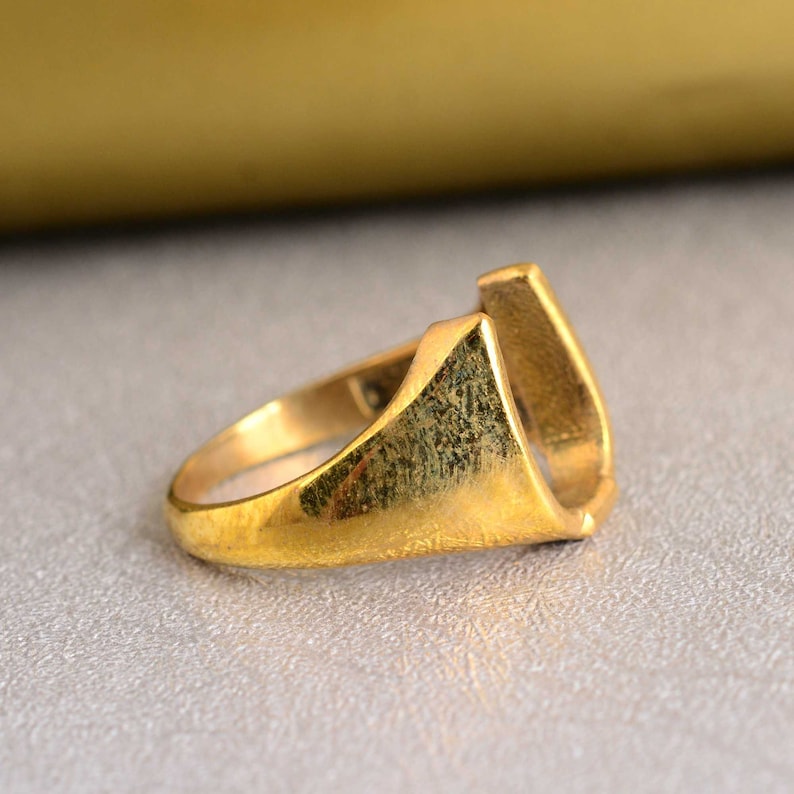 May include: A gold-colored ring shaped like a horseshoe. The ring is thick and has a smooth, polished finish.