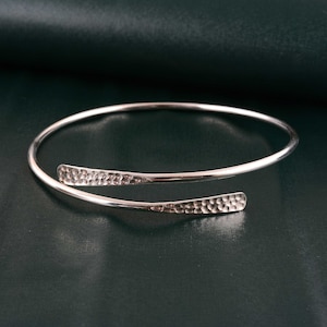 May include: A silver hammered bangle bracelet with a simple, open design.