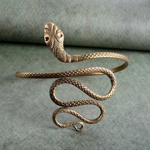 May include: A gold-toned snake-shaped bracelet with a detailed head and a coiled body. The bracelet is made of metal and has a textured finish.