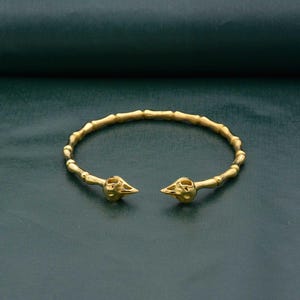May include: A gold bangle bracelet with two skull-shaped ends. The bracelet is made of small, round beads.