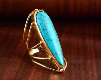 May include: A gold ring with a large turquoise teardrop-shaped stone set in the center. The ring has a delicate, openwork design.