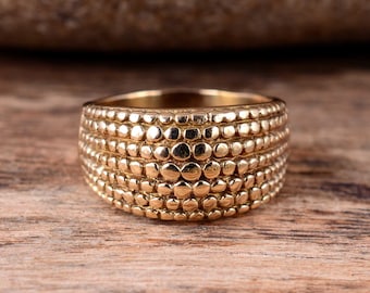 May include: A gold-toned ring with a textured, patterned design. The ring is made of multiple rows of small, round, raised dots.