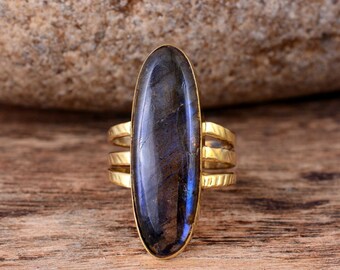 May include: A gold ring with a large oval-shaped labradorite gemstone. The ring has three bands that wrap around the stone.