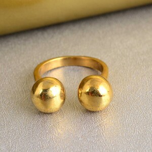 May include: A gold ring with two large round spheres on either side of the band.