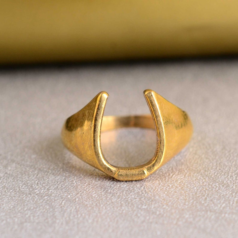 May include: A gold-colored horseshoe ring. The ring is made of metal and has a simple design.