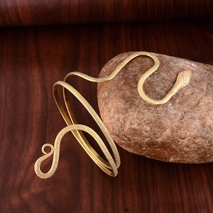 May include: Gold snake-shaped bracelet with a coiled design. The bracelet is made of metal and has a textured finish.