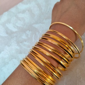 May include: A stack of gold-colored bangles, worn on a person's wrist.