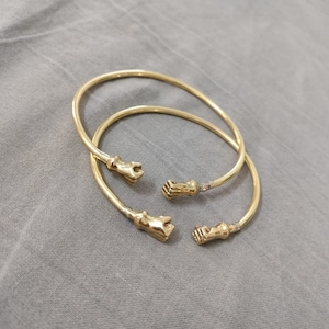 Op de afbeelding: Twee gouden armbanden met handvormige sluitingen. De armbanden zijn eenvoudig en elegant en zouden een geweldig cadeau zijn voor iemand die speciaal is.