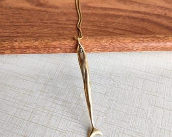 May include: A gold-toned fish pendant necklace with a delicate chain. The pendant is long and slender, with a detailed fish design.