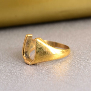 May include: A gold-colored ring with a U-shaped opening. The ring is made of metal and has a smooth, polished finish.