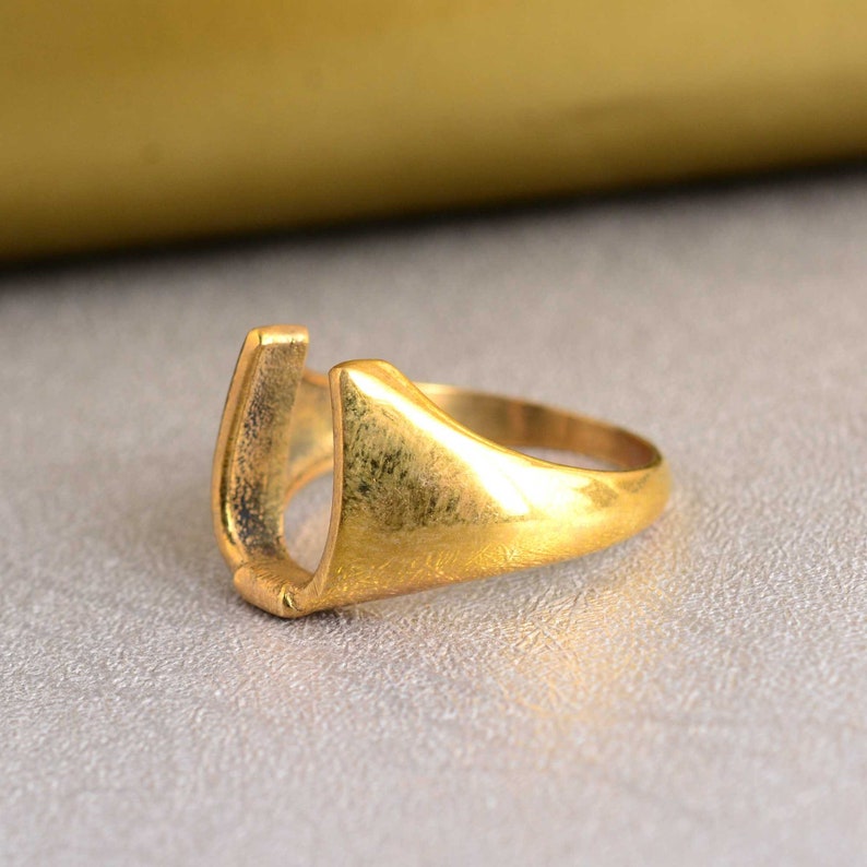 May include: A gold-colored ring with a U-shaped opening. The ring is made of metal and has a smooth, polished finish.