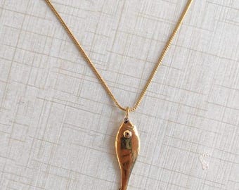 May include: A gold chain necklace with a gold fish pendant. The fish has a small round eye.