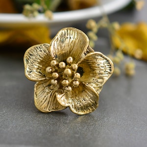 May include: A gold-colored metal flower with a textured surface. The flower has five petals and a center with small, round details.