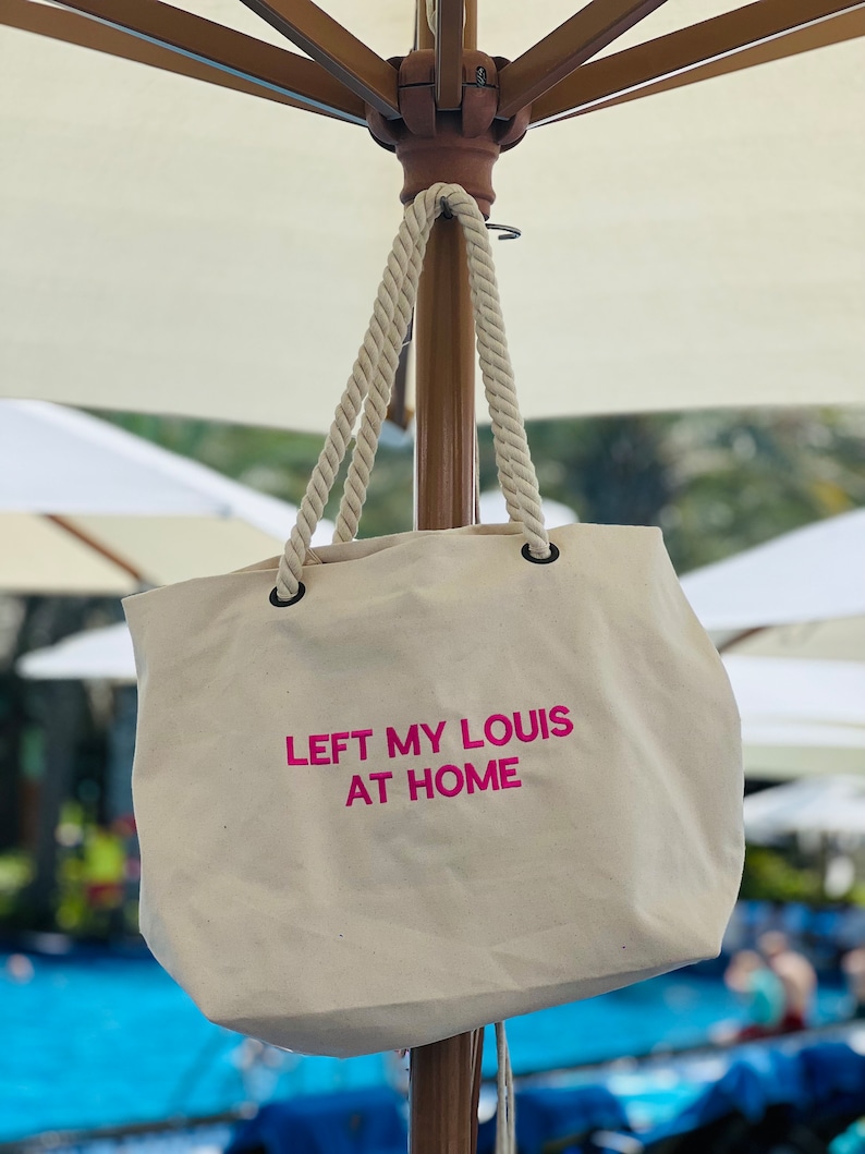 May include: A white canvas tote bag with pink rope handles and the text "LEFT MY LOUIS AT HOME" printed in pink.