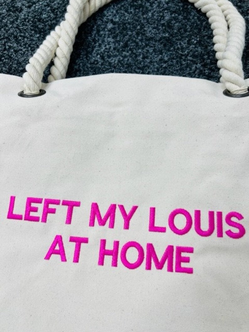 May include: White canvas tote bag with rope handles and pink embroidered text that reads "LEFT MY LOUIS AT HOME".