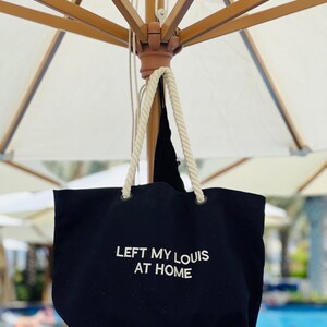 May include: A black canvas tote bag with white rope handles. The bag has the text "LEFT MY LOUIS AT HOME" embroidered on the front.