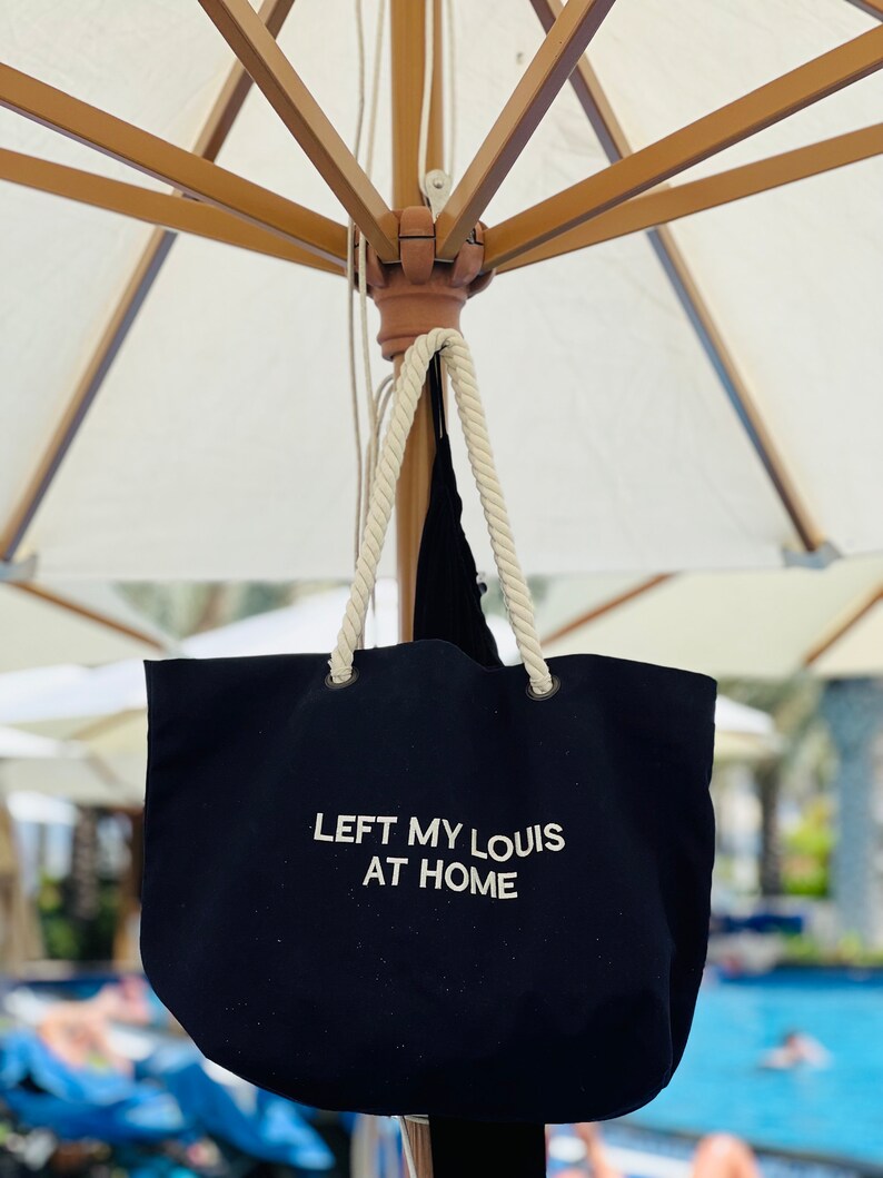 May include: A black canvas tote bag with white rope handles. The bag has the text "LEFT MY LOUIS AT HOME" embroidered on the front.