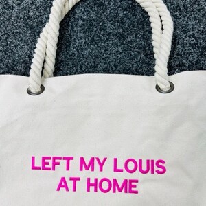May include: White canvas tote bag with thick white rope handles. The bag has pink embroidered text that reads "LEFT MY LOUIS AT HOME".