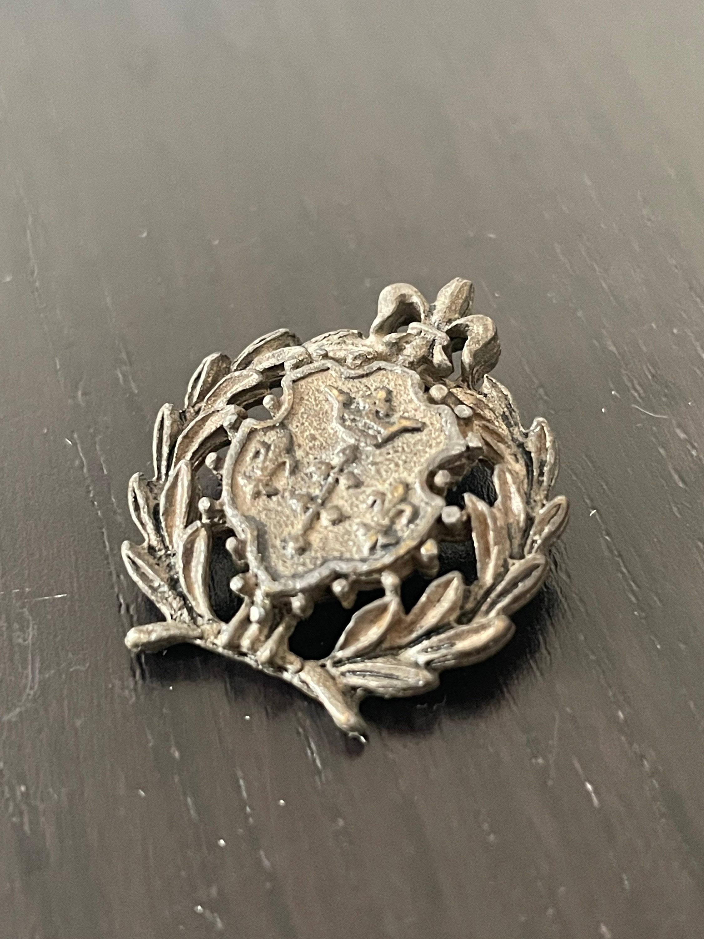 Insignia antigua de metal con corona militar pequeña y flor de lis