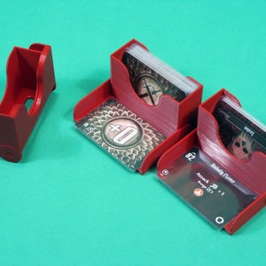 May include: Three red plastic card holders with clear plastic inserts for holding playing cards. The cards have black and white illustrations and text. The text on one card reads "Unholy Flame" and "Attack +1 Range x3".