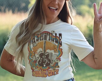 May include: A white t-shirt with a retro graphic design featuring a guitar, cityscape, and the text "Nashville Music City". The model is wearing a straw hat and smiling.