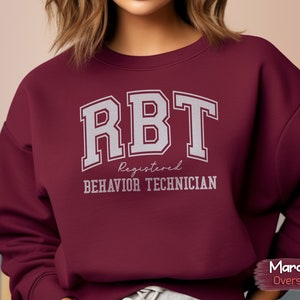 May include: Maroon oversized sweatshirt with the text "RBT Registered Behavior Technician" in white.