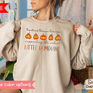 May include: Beige sweatshirt with the text "Registered Behaviour Technician supporting the cutest LITTLE PUMPKINS" and four cartoon pumpkins with different facial expressions.