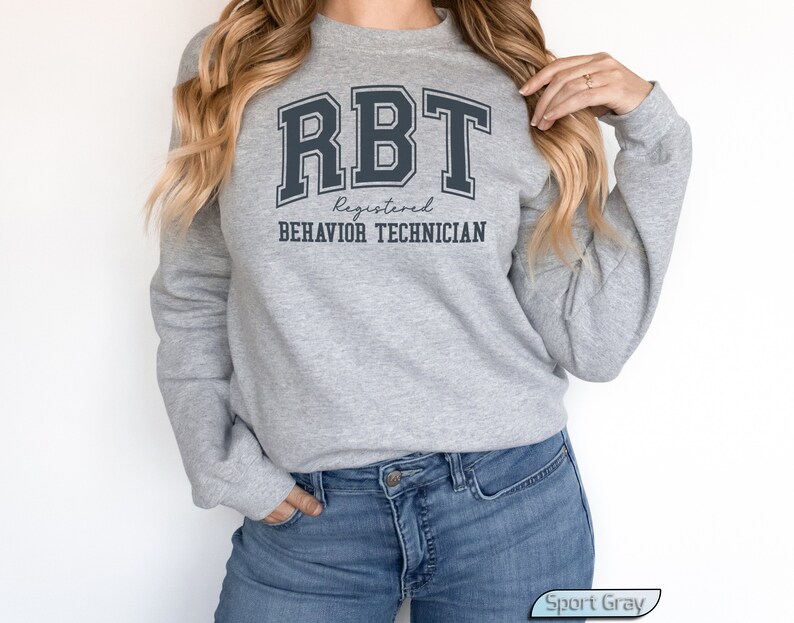 May include: A gray sweatshirt with the text "RBT Registered Behavior Technician" in black lettering. The sweatshirt is being worn by a person with long blonde hair.