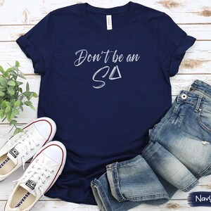 T-shirt featuring text Don't be an S Delta in a paintbrush font. Playful reminder for Registered Behavior Technicians (RBTs) and Applied Behavior Analysis (ABA) therapists.