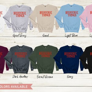 May include: A variety of colors of sweatshirts with the text "BEHAVIORAL THINGS" printed in red on the front. The text is in a bold, sans-serif font and is enclosed in a red rectangle. The sweatshirts are available in white, sport grey, sand, light blue, light pink, maroon, dark heather, forest green, navy, and black.