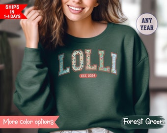 May include: Forest green sweatshirt with the word "LOLLI" in floral patterned letters. The text "EST. 2024" is below the word "LOLLI".