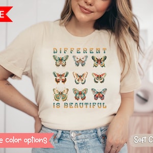 May include: A cream colored t-shirt with a graphic of colorful butterflies and the text "Different is Beautiful".