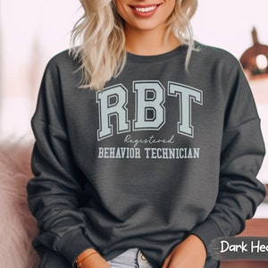 May include: Dark heather grey sweatshirt with the text "RBT Registered Behavior Technician" in a light blue color with a varsity style font.