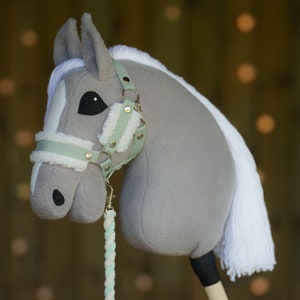 May include: A gray and white stuffed horse head with a light green and white bridle. The horse has a white mane and tail.