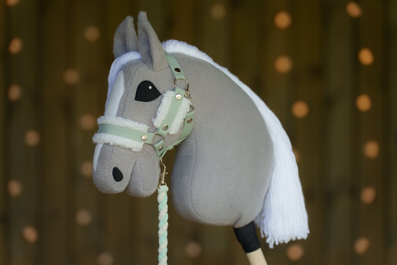May include: A gray and white stuffed horse head with a light green and white bridle. The horse has a white mane and tail.
