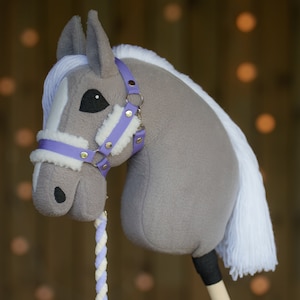 May include: A gray and white stuffed horse head with a purple halter and a white mane. The horse is on a wooden stick with a white and purple rope attached.