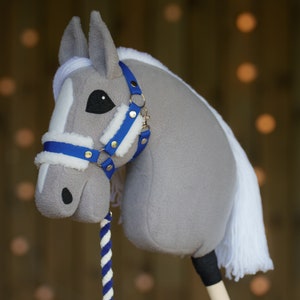 May include: A gray and white stuffed horse head with a blue and white bridle. The horse has a white mane and tail. The horse is on a wooden stick.