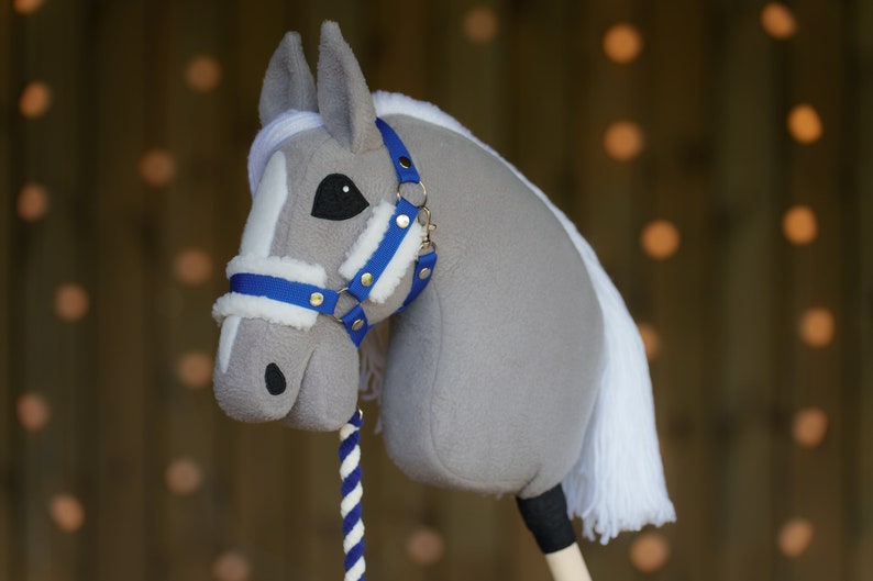 May include: A gray and white stuffed horse head with a blue and white bridle. The horse has a white mane and tail. The horse is on a wooden stick.