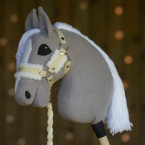 May include: A gray and white plush rocking horse head with a beige leather bridle and gold accents. The horse has a white mane and tail.