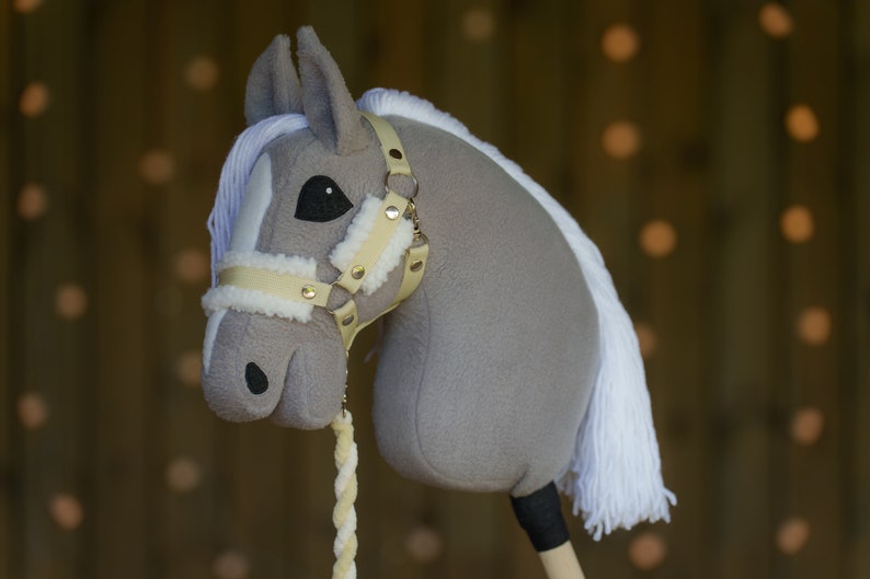 May include: A gray and white plush rocking horse head with a beige leather bridle and gold accents. The horse has a white mane and tail.