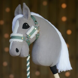 May include: A gray and white plush rocking horse with a green and gold bridle. The horse has a white mane and tail.