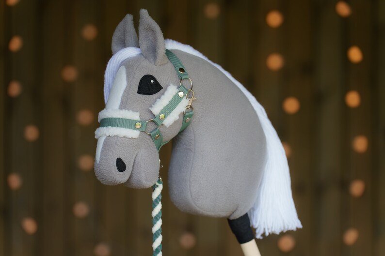 May include: A gray and white plush rocking horse with a green and gold bridle. The horse has a white mane and tail.